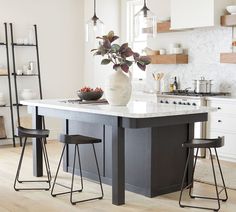 a kitchen island with three stools and a vase on it in front of the counter