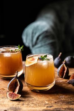 two glasses filled with liquid sitting on top of a wooden table next to figs