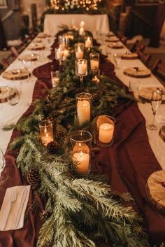 a long table is set with candles and evergreen garland for a festive dinner party