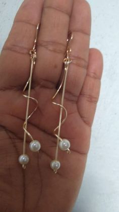 a pair of gold earrings with pearls hanging from it's ear wires on a person's hand