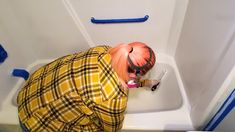 a person in yellow and black clothing using a paint roller on a bathtub with blue handles