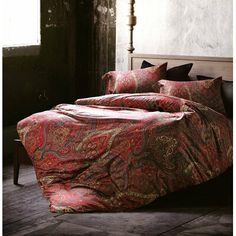 a bed covered in a red paisley comforter next to a window