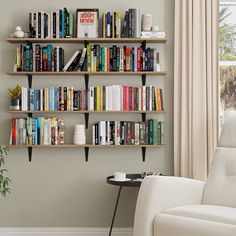 a living room filled with lots of books on shelves next to a white chair and window