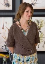 a woman standing in front of two paintings wearing a brown sweater and multicolored dress