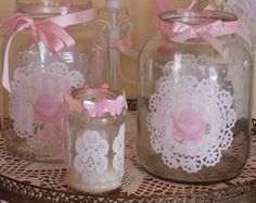 three glass jars with doily and pink roses on them are sitting on a table