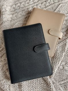 two notebooks sitting next to each other on top of a white and black blanket