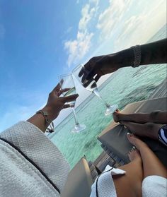 two people toasting with wine glasses in front of the ocean on a sunny day