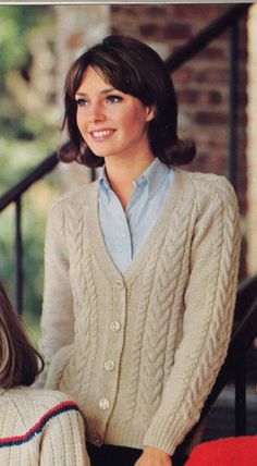 a woman wearing a sweater and cardigan sitting on a chair in front of stairs