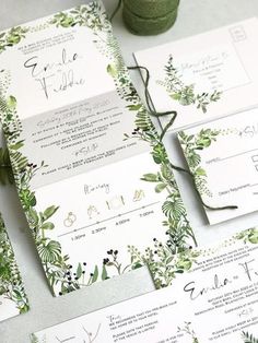 the wedding stationery is laid out on top of each other, with greenery