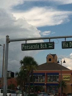 two green street signs hanging from the side of a traffic light over a parking lot