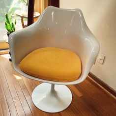 a white chair with a yellow cushion sitting on top of a wooden floor next to a potted plant