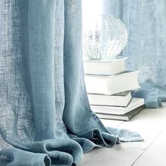 a stack of books sitting on top of a wooden floor next to a window covered in blue curtains