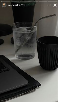 a laptop computer sitting on top of a desk next to a glass filled with water