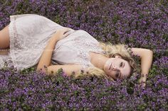 a woman laying in the middle of a field of flowers wearing a white lace dress