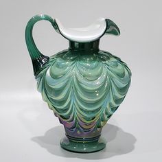 a green and white glass vase sitting on top of a table next to a wall