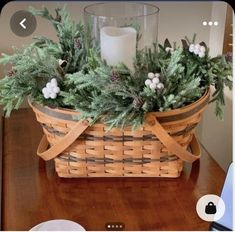 a basket filled with greenery on top of a wooden table next to a candle