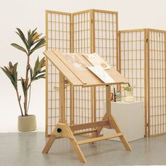 a wooden easel sitting in front of a screen and potted plant next to it