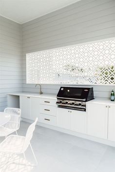 an outdoor kitchen with white cabinets and counter tops is pictured in this image, there are two chairs near the stove