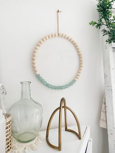 a white shelf with a glass vase and wooden bead ring hanging on the wall