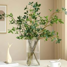 a vase filled with greenery on top of a table next to a cup and saucer