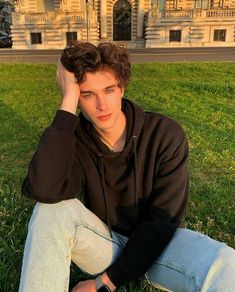 a young man sitting on the grass in front of a building