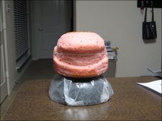 a pink donut sitting on top of a piece of tin foil covered in frosting