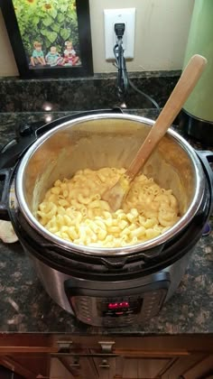 a large pot filled with macaroni and cheese on top of a counter next to a wooden spoon