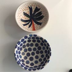 two bowls with designs on them sitting next to each other, one has a palm tree painted on it