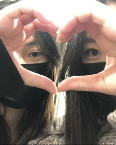 a woman making a heart shape with her hands while wearing a black mask on top of her head