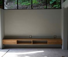 an empty room with a large window and wooden shelf on the wall next to it