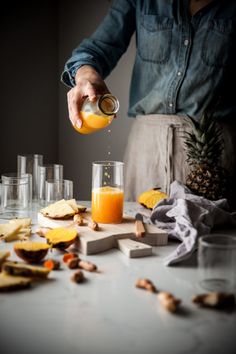 a person pouring orange juice into glasses on a table with pineapples and other ingredients