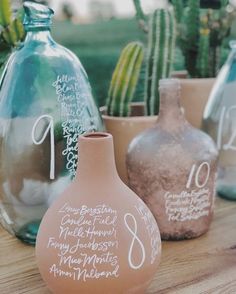 three vases with writing on them sitting on a table next to cacti