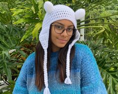 a woman wearing a blue sweater and white knitted bear hat with pom poms