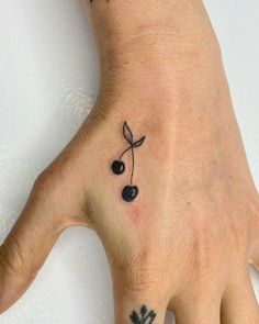 a person's hand with a small black cherry tattoo on the left side of their ring finger