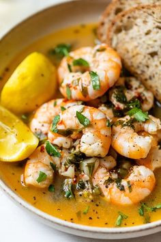 a bowl filled with shrimp and bread next to a slice of lemon on top of a table