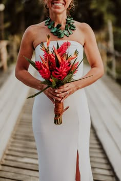 a woman in a white dress holding a bouquet of flowers and smiling at the camera