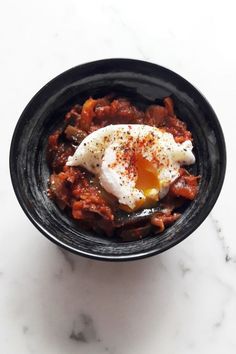 a black bowl filled with food on top of a white marble countertop and topped with an egg