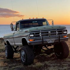 an old pick up truck parked on the side of a hill near the ocean at sunset