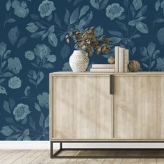 a vase with flowers on top of a wooden cabinet in front of a blue floral wallpaper