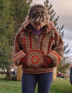 a woman standing in the grass wearing a crocheted jacket