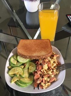 a white plate topped with toast, cucumbers and scrambled eggs next to a glass of orange juice