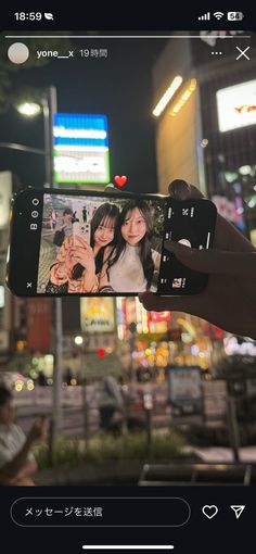 someone holding up their cell phone to take a photo in front of a city street at night