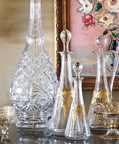 an assortment of glass vases and glasses on a table in front of a painting