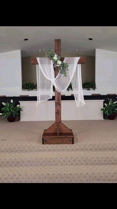 a wooden cross with flowers on it in front of a church pew and flower arrangement