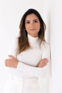 a woman with her arms crossed standing in front of a white wall and looking at the camera