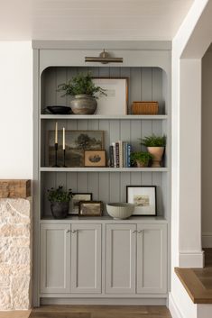 a bookcase with books and plants on it in a living room next to a fireplace