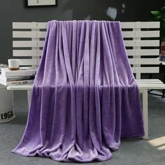 a purple blanket sitting on top of a wooden bench next to a white table and chair