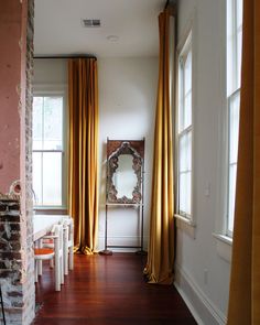 a living room filled with furniture and windows covered in yellow draping next to a brick wall