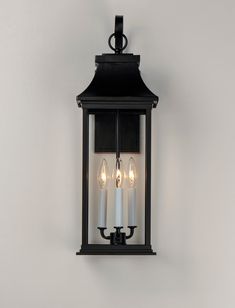 a wall mounted light with three candles on the front and back of it, against a white wall