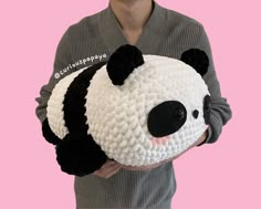 a person holding a stuffed panda bear in front of a pink background and wearing a gray sweater